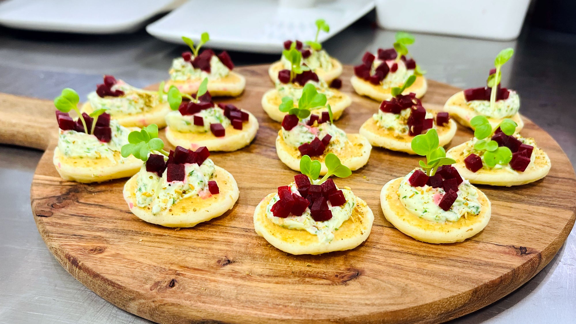 Fresh meal canapés — blinis topped with herb cream and beetroot on a wooden board